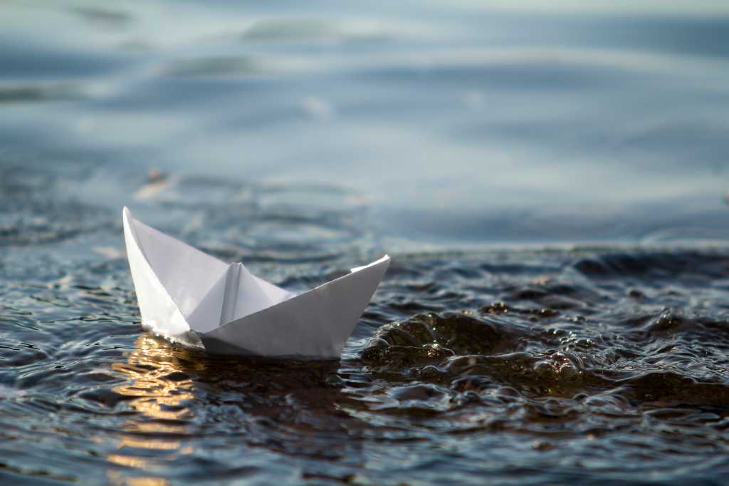 Stop mimicking and start anchoring Close-up of simple small white origami paper boat floating in blue clear river or sea water under bright summer sky. Beauty of nature, freedom, dreams and fantasies concept.