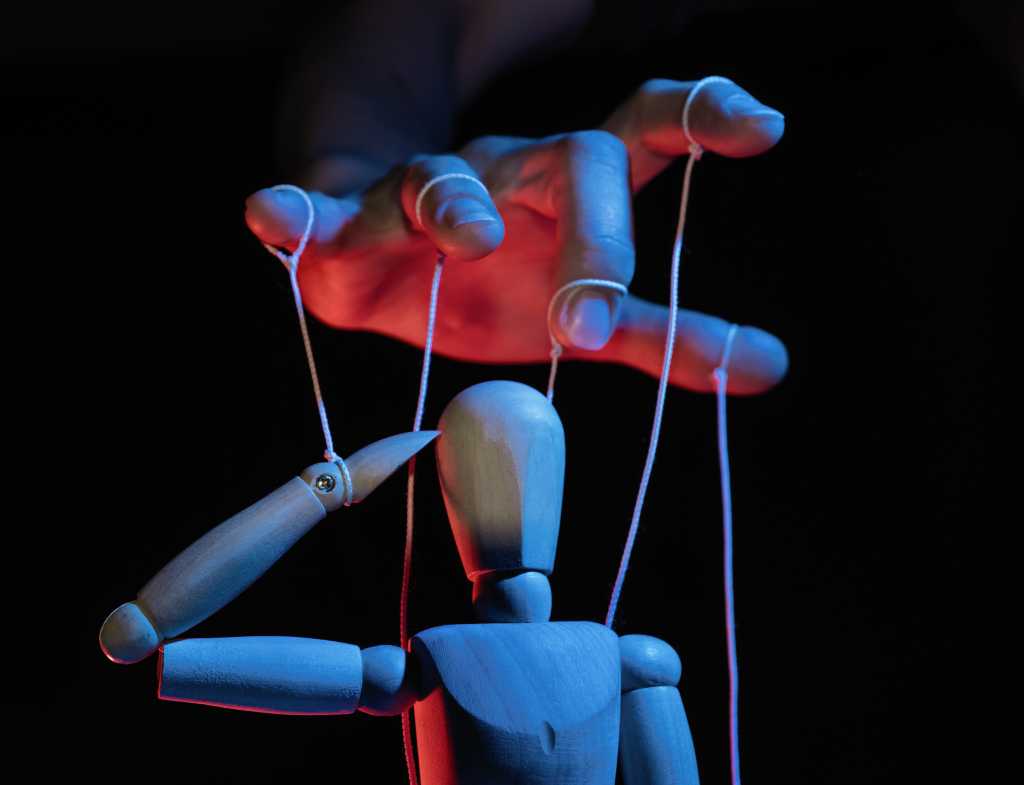Why the CIO is becoming the chief autonomy officer Concept of control. Marionette in human hand. Objects are colored on red and blue light.