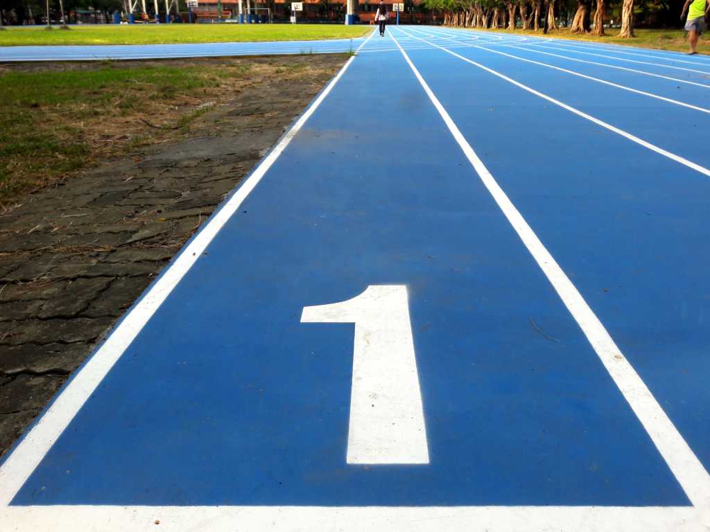 ‘Futuristic’ Unison functional language debuts Number 1 / number one lane of running track, white number and white lane lines on blue surface. Low level view with grass runners trees visible in the distance.