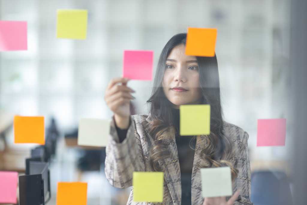 10 top priorities for CIOs in 2026 Business female employee with many conflicting priorities arranging sticky notes commenting and brainstorming on work priorities colleague in a modern office.