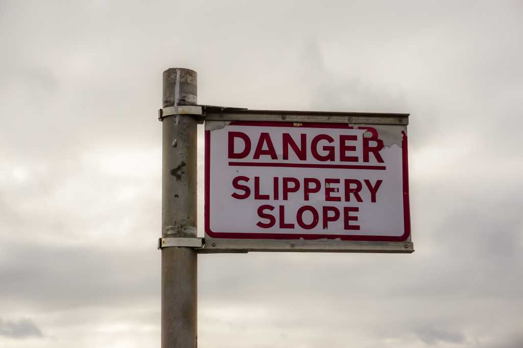 AI agents and bad productivity metrics Sign post reading, Danger Slippery Slope. Warning sign near seafront on overcast day.