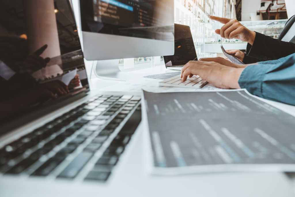 Visual Studio Code 1.115 introduces VS Code Agents app Developers work together to review lines of code in an office workspace.