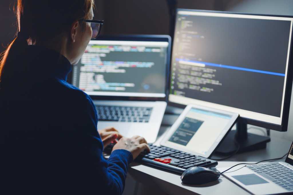 As AI speeds coding, CVE Lite CLI keeps security deliberately AI-free Young Asian woman, developer programmer, software engineer, IT support, wearing glasses working hard at nitght overtime on computer to check coding in bugging system. Back view