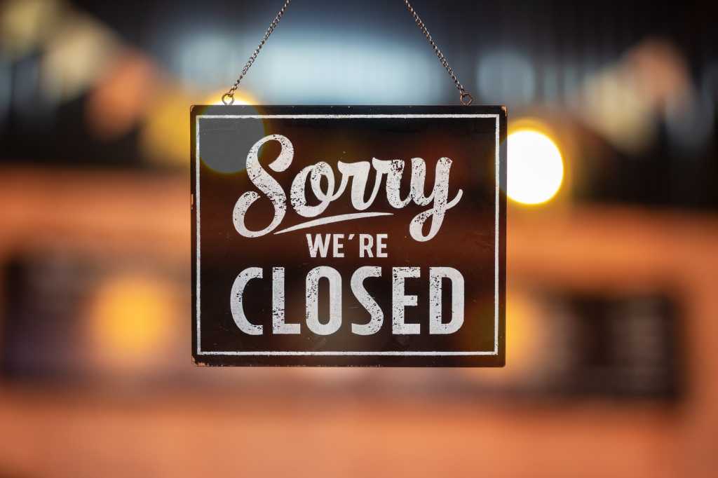 Open source grapples with agentic coding Sorry we're closed sign hanging inside a glass door, colored lights in the background.