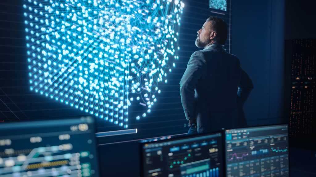 The next AI breakthrough won’t come from bigger models, but from better data Middle Aged Bearded Senior Project Manager Stands Next to Big Screen with Neural Network. Professional Computer Data Science Engineer Work in a System Control and Monitoring Telecommunications Office