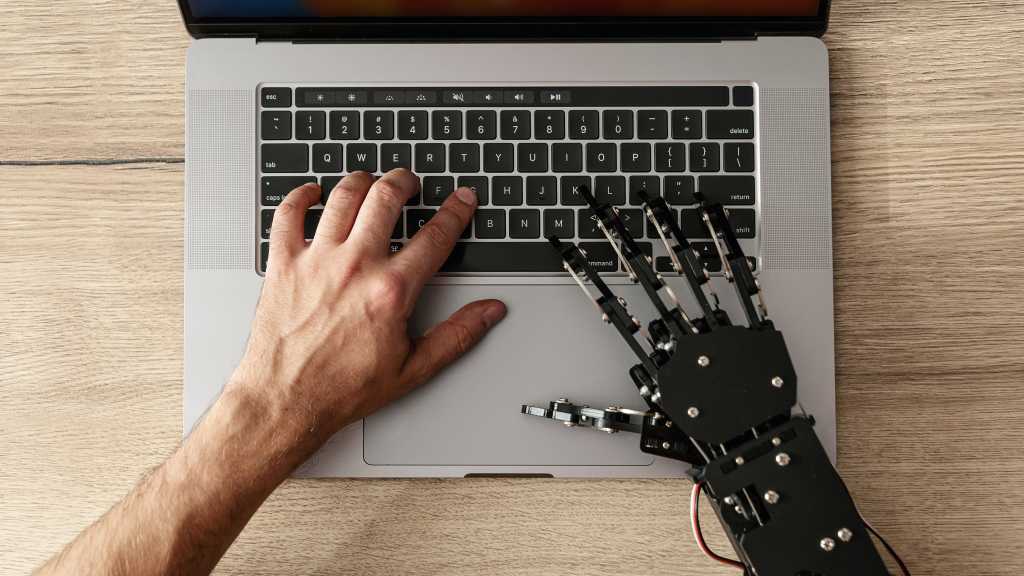 SpaceXAI launches Grok 4.5, touts lower coding-task costs than AI rivals image of a human and robot hand typing at a laptop